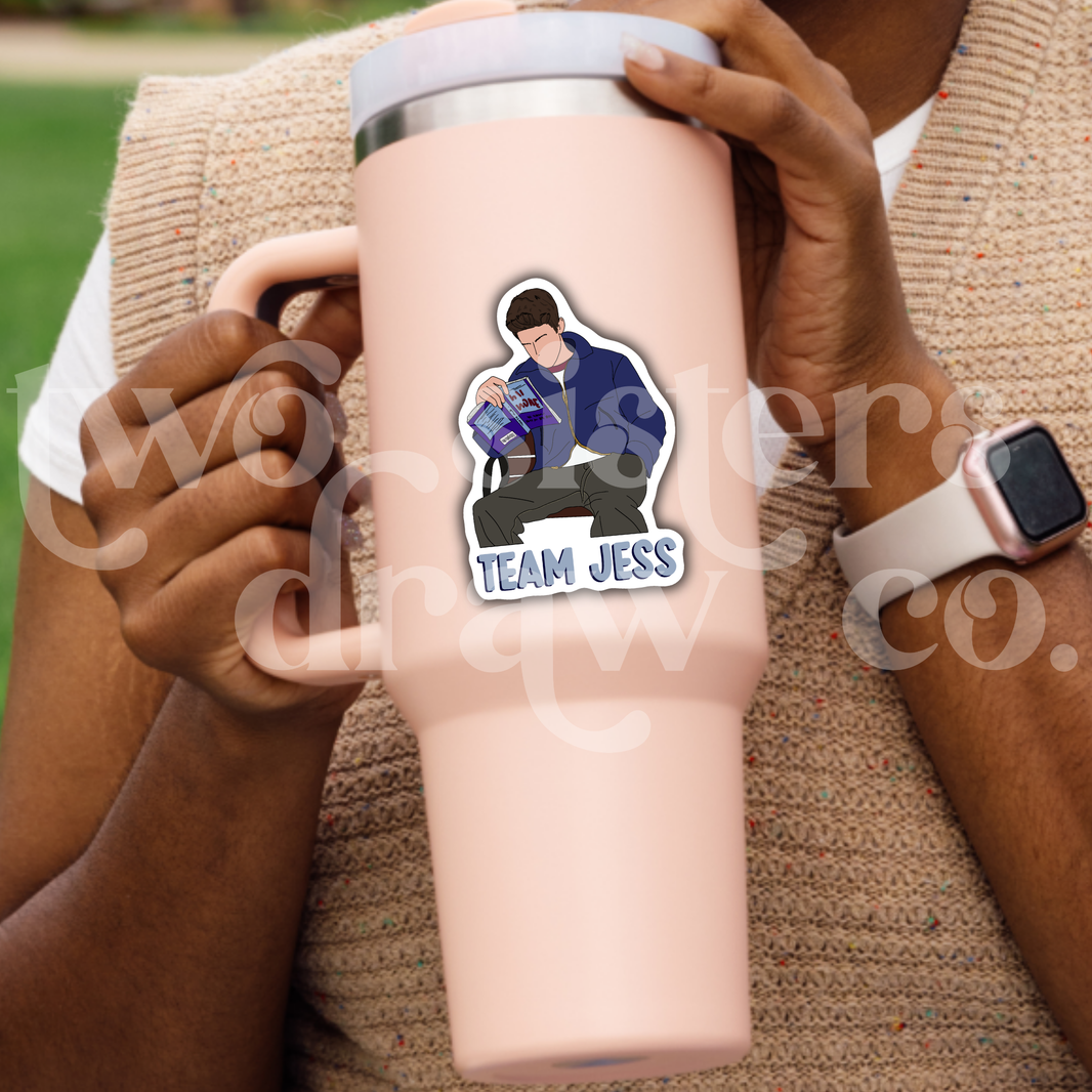Person holding a tumbler with a sticker of Jess Mariano sitting on a bench reading with 'Team Jess' text.