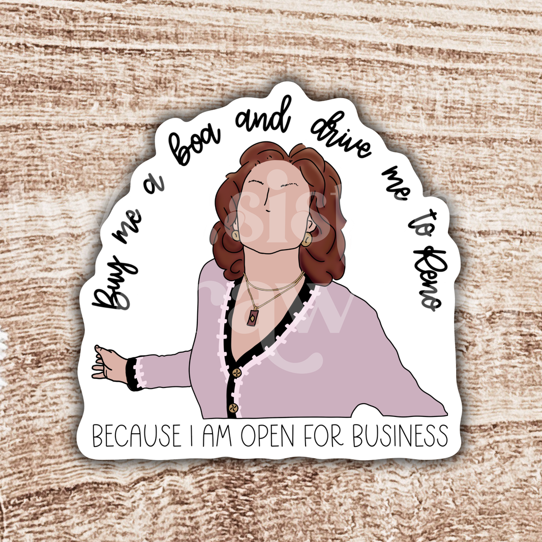 Illustrated Emily Gilmore sticker with "buy me a boa and drive me to Reno because I am open for business" quote in black script on a white background in front of a wood grain background.
