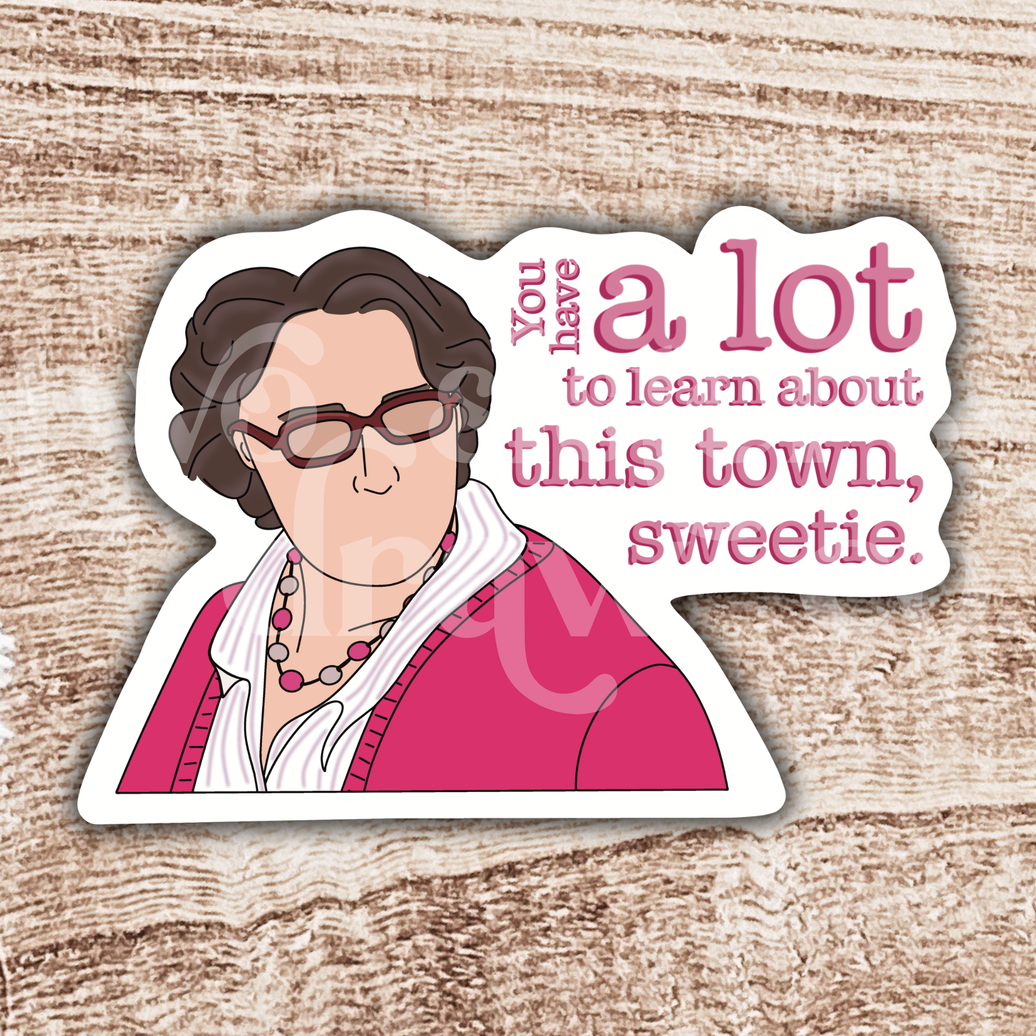 Hand-drawn sticker of Phyllis Vance from The Office in a pink outfit and glasses with the text ‘you have a lot to learn about this town, sweetie’ on a wooden background.