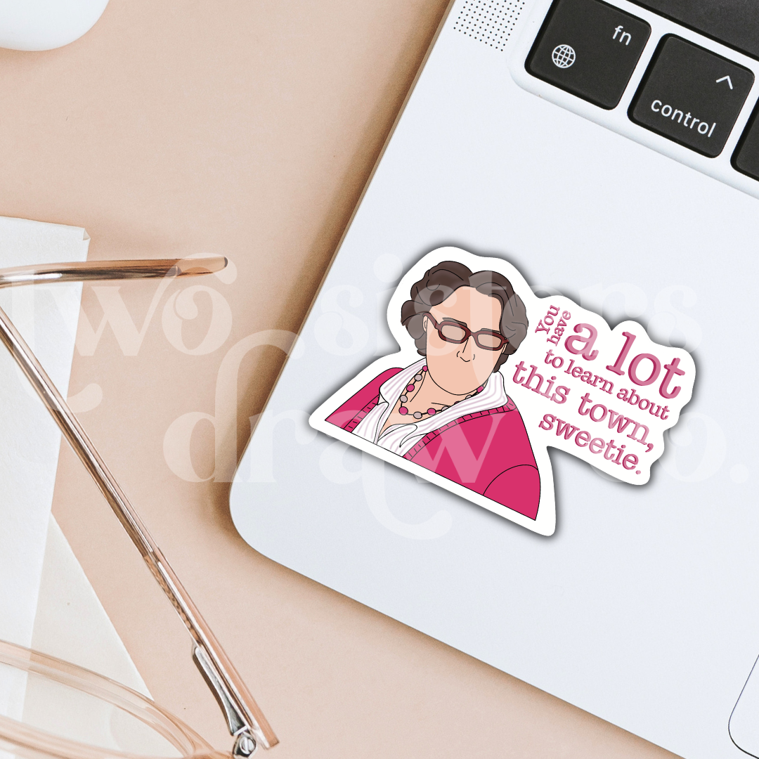 Hand-drawn sticker of Phyllis Vance from The Office in a pink outfit and glasses with the text ‘you have a lot to learn about this town, sweetie’ on a laptop.