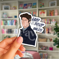 Erin holding an hand-drawn Jess Mariano sticker with the text ‘why did you drop out of Yale?!’ beside him in front of a book case.