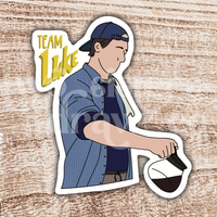 Hand-drawn sticker of Luke Danes pouring coffee with the test ‘Team Luke’ with a wooden background. 
