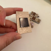 Hand holding a polymer clay magnet showing the adhesive, ferrite magnet secured to the back, with additional magnets behind on a white background.