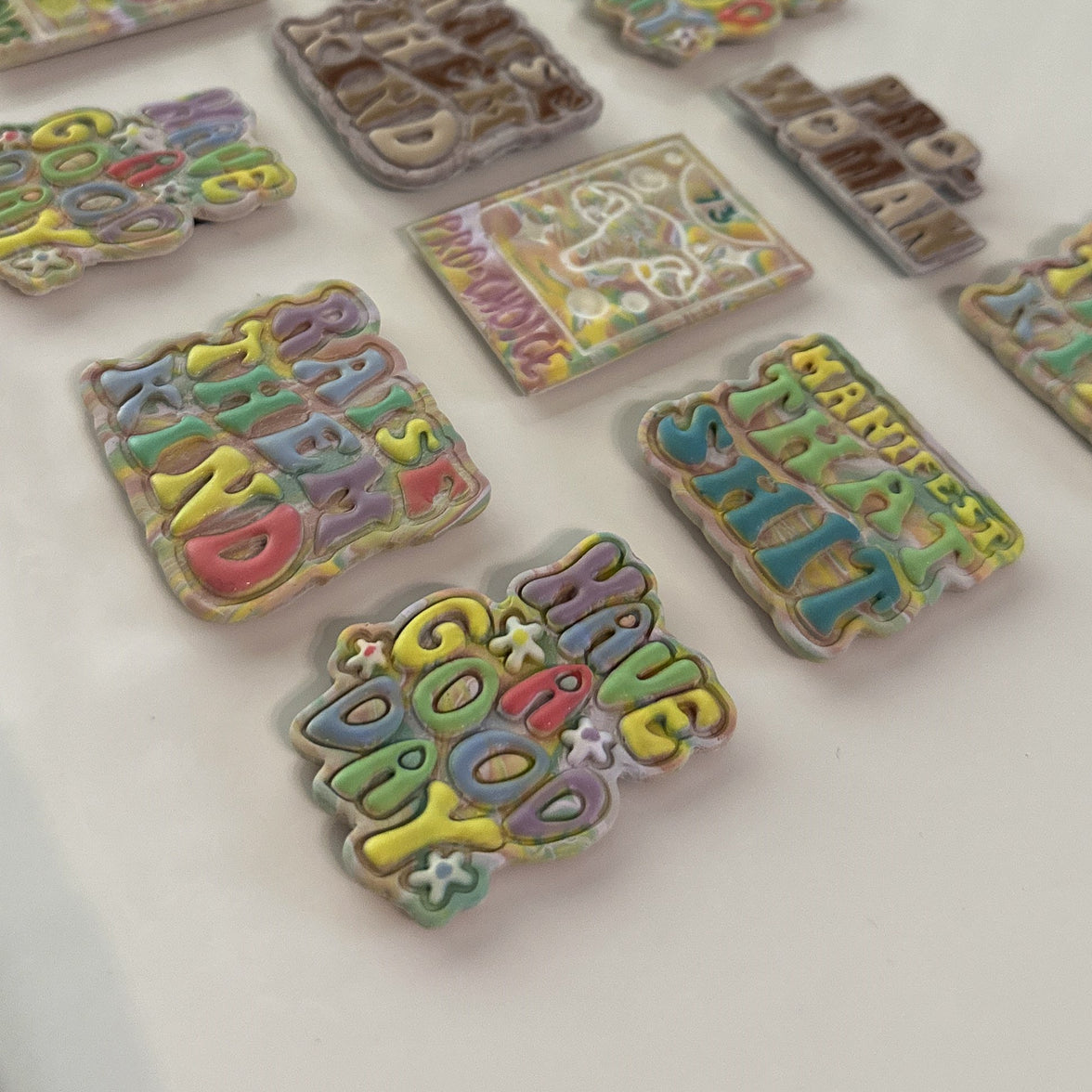 Close-up of handmade, polymer clay magnets featuring 3D bubble lettering in sherbet and neutral color palettes on a white background.